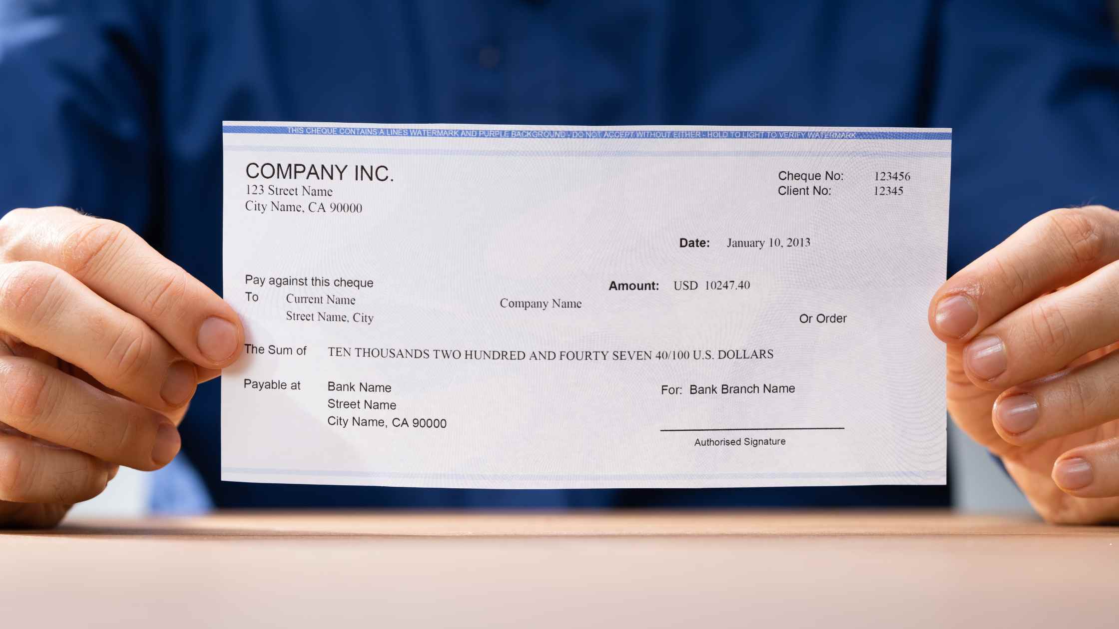 Close-up of a bank cheque with security features including watermarks and microprint, placed on a desk alongside a pen and financial