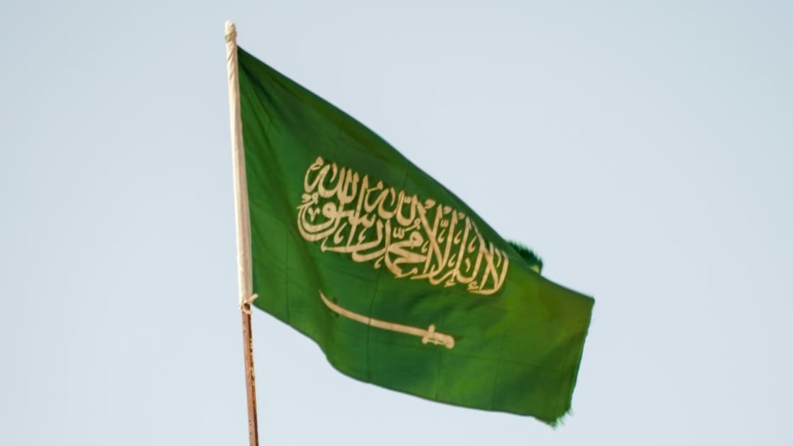 Close-up of a Saudi Arabian passport placed on a desk next to a laptop displaying the SIMAH credit bureau portal interface and official