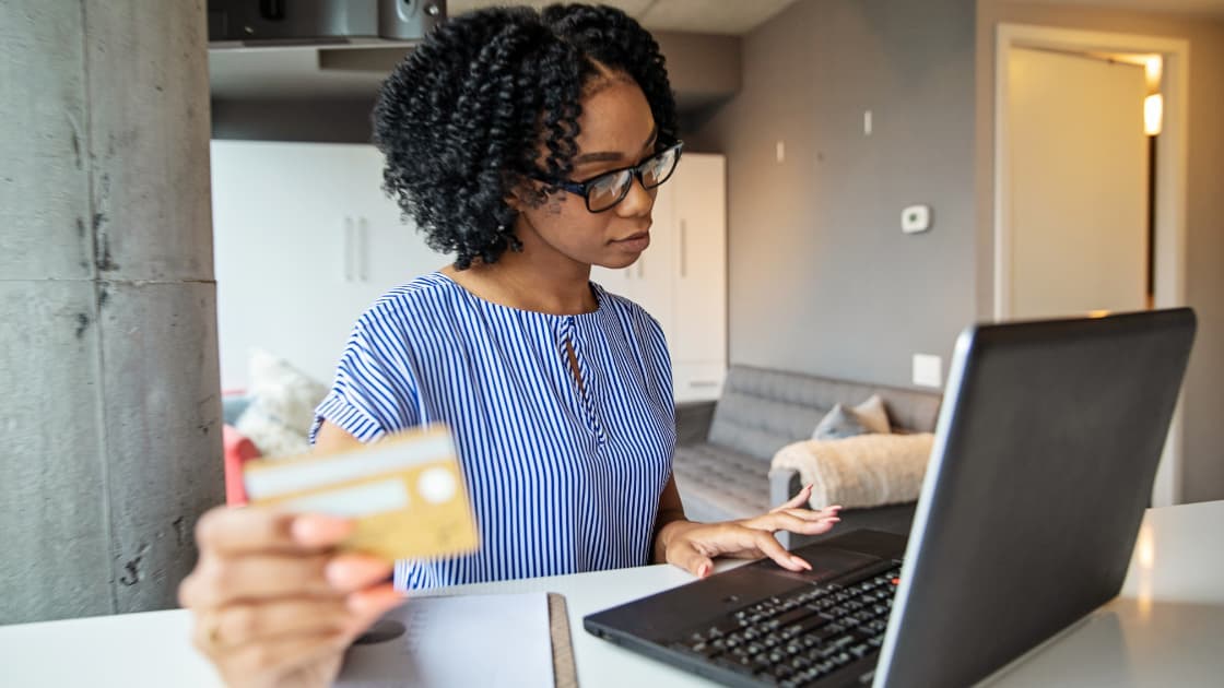 Close-up of a declined payment card being held in front of a laptop screen displaying a frozen bank account notification
